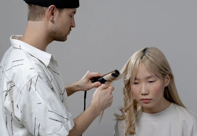 A hairstylist using a curling iron to style a woman's hair in a salon setting