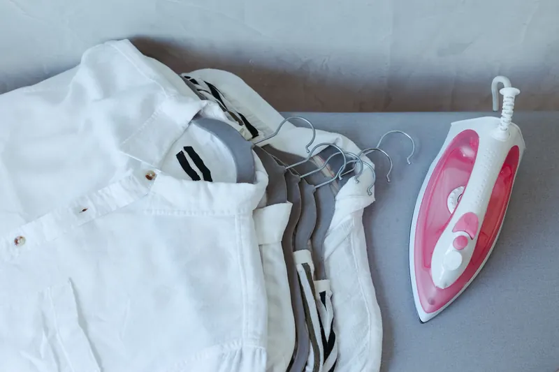 A flat lay of folded white shirts with a pink iron, illustrating sleek home care