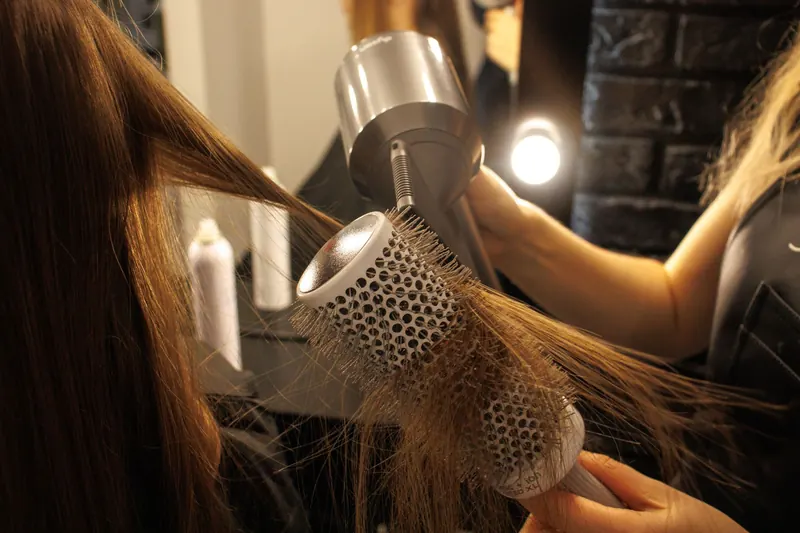 Close-up of a hairstylist drying and styling long hair with a round brush in a salon