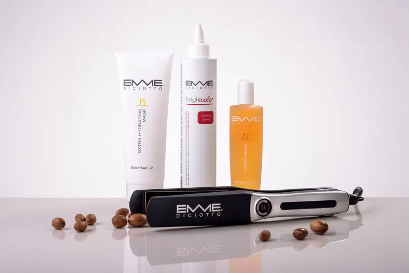 Hair care products and a flat iron by EMME Diciotto on a reflective surface for beauty routines