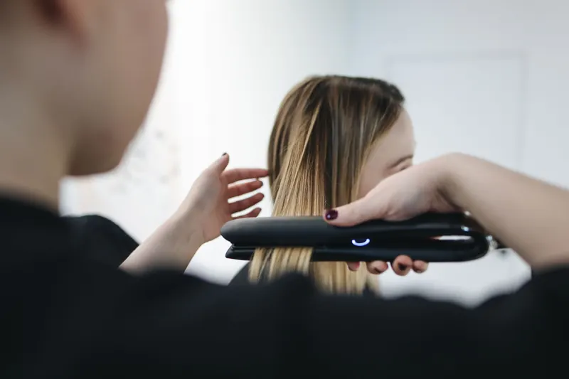 Close-up of a hairstylist using a straightening iron for sleek hairstyle indoors