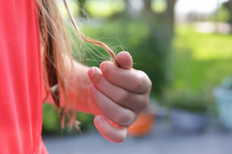 A young girl gently holds a strand of hair, showcasing a serene outdoor moment