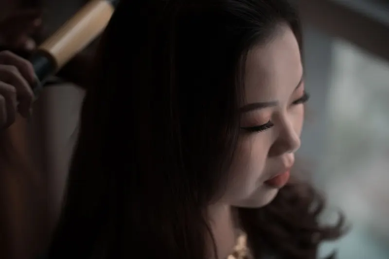 Close-up of an Asian woman having her hair styled with a curling iron indoors