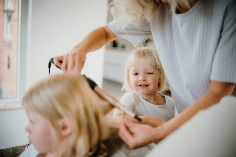 A woman styling her child's hair with a curling iron, creating a warm family bonding moment