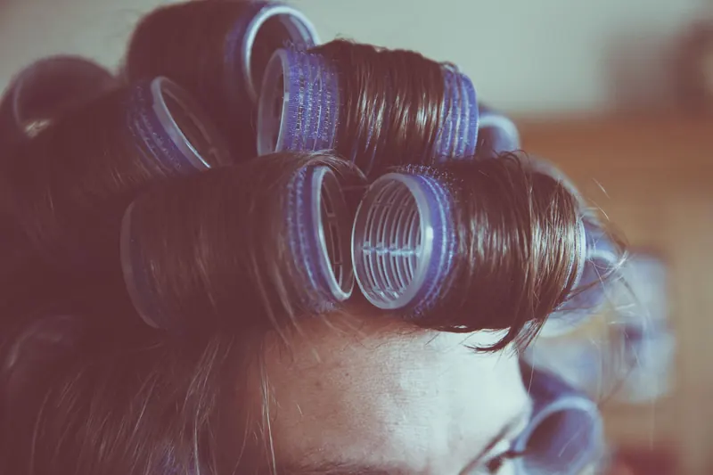 Vintage-style close-up of a woman's hair in curlers, emphasizing retro hair styling
