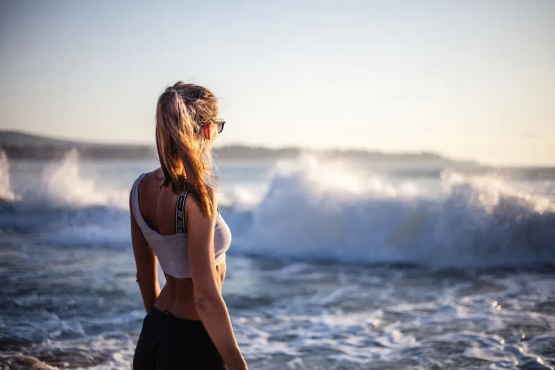 Back view of a woman enjoying the ocean waves on a beach during sunset
