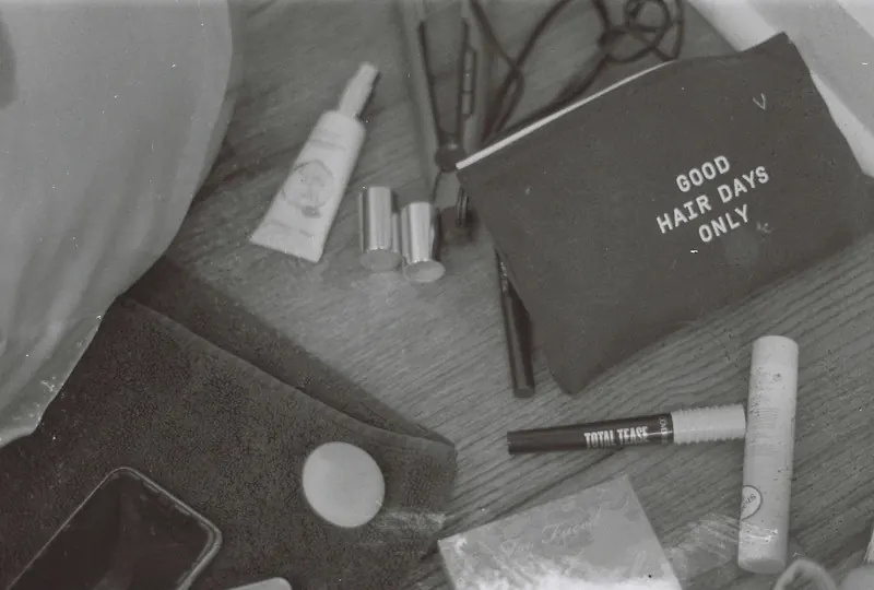 Flat lay of cosmetics and hair essentials on a wooden surface in monochrome