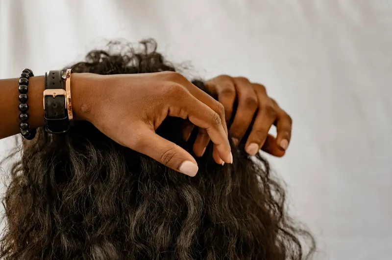 Detailed image of hands styling curly hair, showcasing accessories and a natural hairstyle