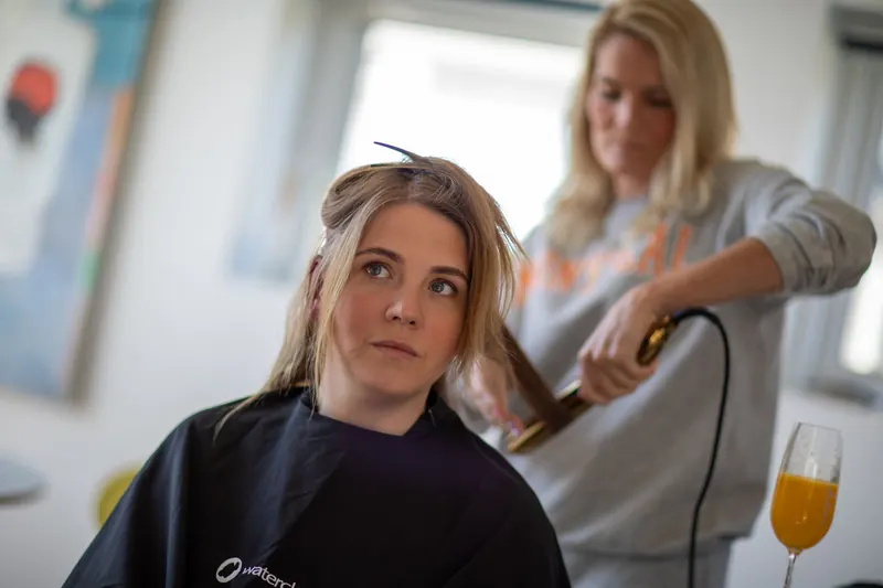 Woman in salon cape receiving professional hair styling indoors by hairdresser