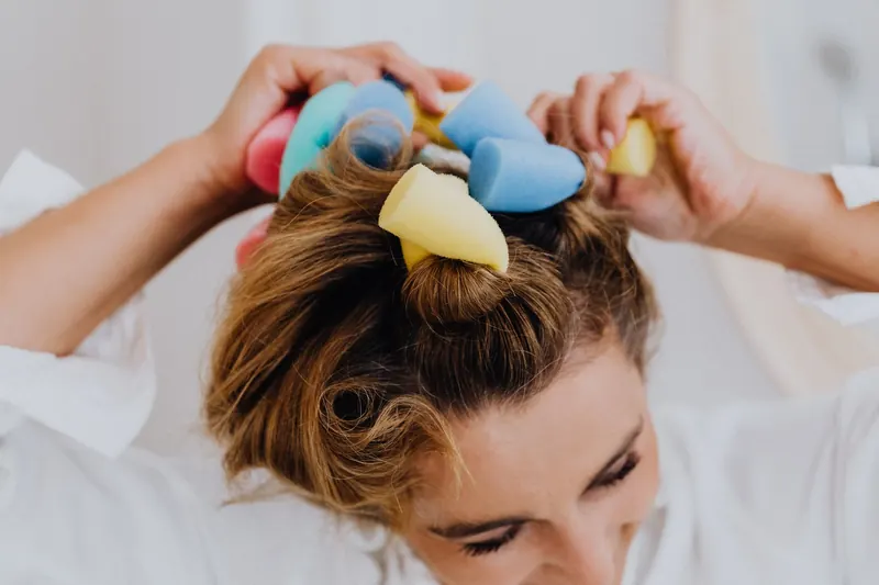 Close-up of a woman using colorful foam rollers to style her hair indoors