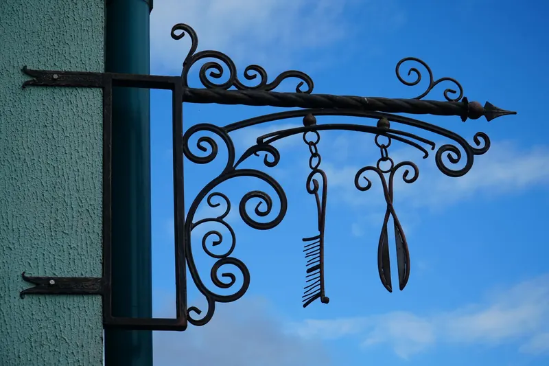 Intricate wrought iron sign with styling tools against a clear blue sky in Pinsk, Belarus
