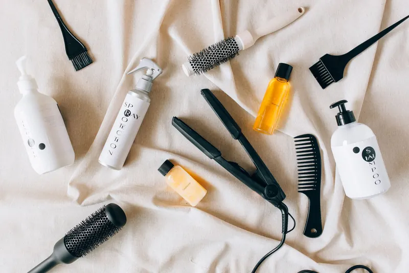 Flat lay image of various hair care products and tools on a textured fabric surface